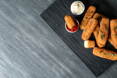 Photo of Board with cheese sticks and sauces on table, top view. Space for text