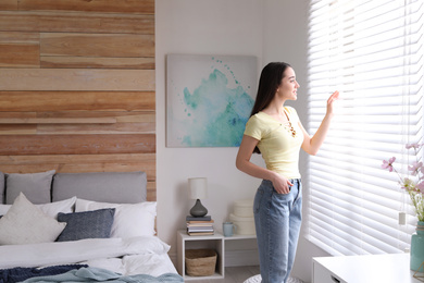 Photo of Young woman near window in modern bedroom. Elegant interior