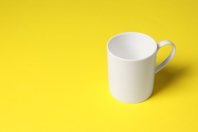 Photo of One white ceramic mug on yellow background, space for text