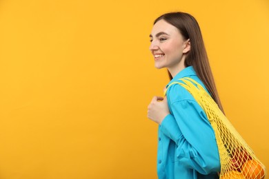 Photo of Woman with string bag of fresh oranges on orange background, space for text