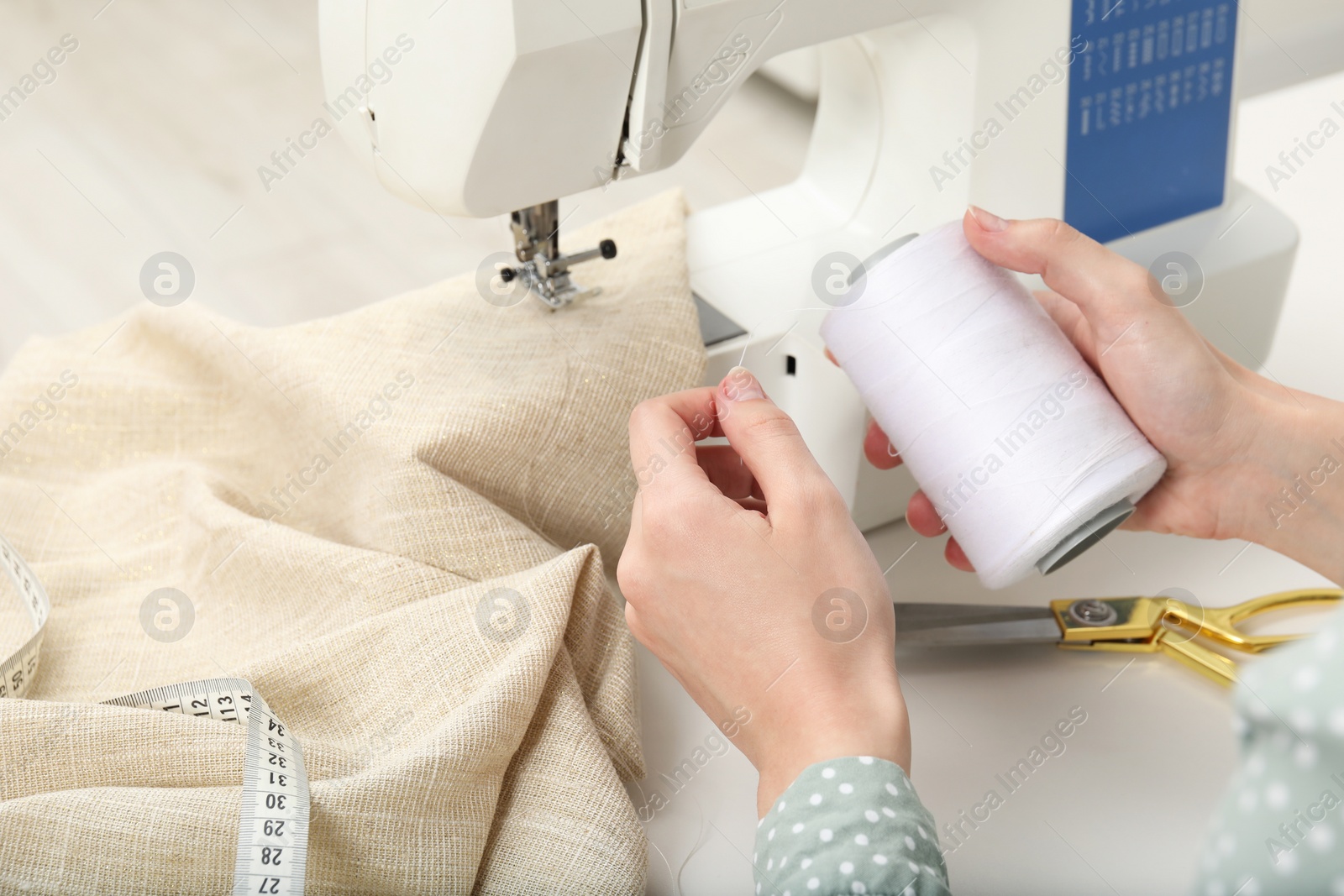 Photo of Seamstress working with sewing machine at table indoors, closeup