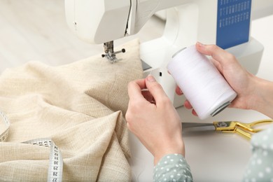 Photo of Seamstress working with sewing machine at table indoors, closeup