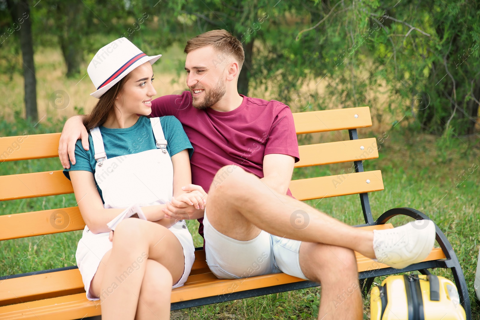 Photo of Beautiful young couple with suitcase packed for summer journey sitting on bench