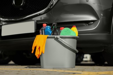 Car cleaning products in bucket near automobile outdoors on sunny day