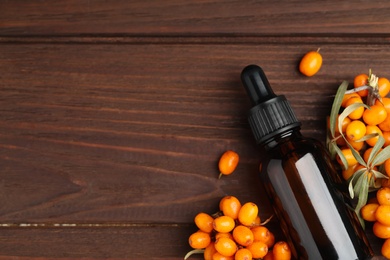 Natural sea buckthorn oil and fresh berries on wooden table, flat lay. Space for text