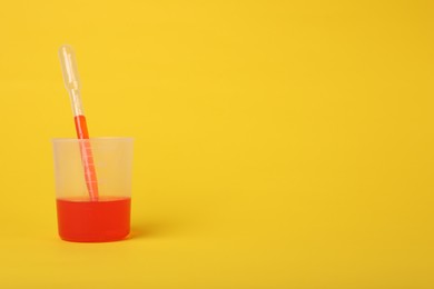 Photo of Beaker with liquid and stirring rod on yellow background, space for text. Kids chemical experiment toy