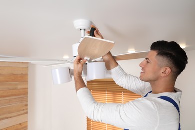 Photo of Electrician with screwdriver repairing ceiling fan indoors