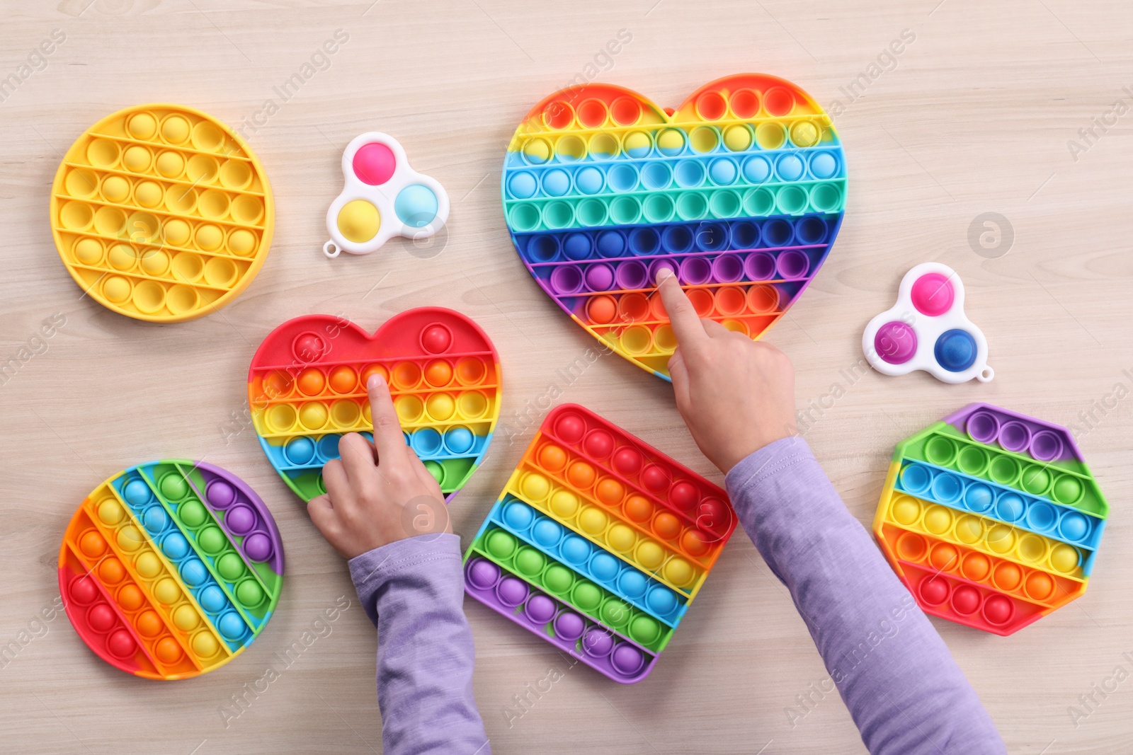 Photo of Little child playing with pop it and simple dimple fidget toys at wooden table, top view