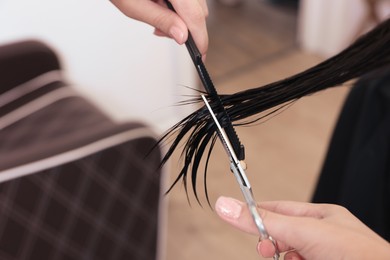 Photo of Professional hairdresser cutting woman's hair in beauty salon, closeup