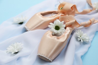 Photo of Ballet shoes. Elegant pointes, flowers and cloth on light blue background, closeup