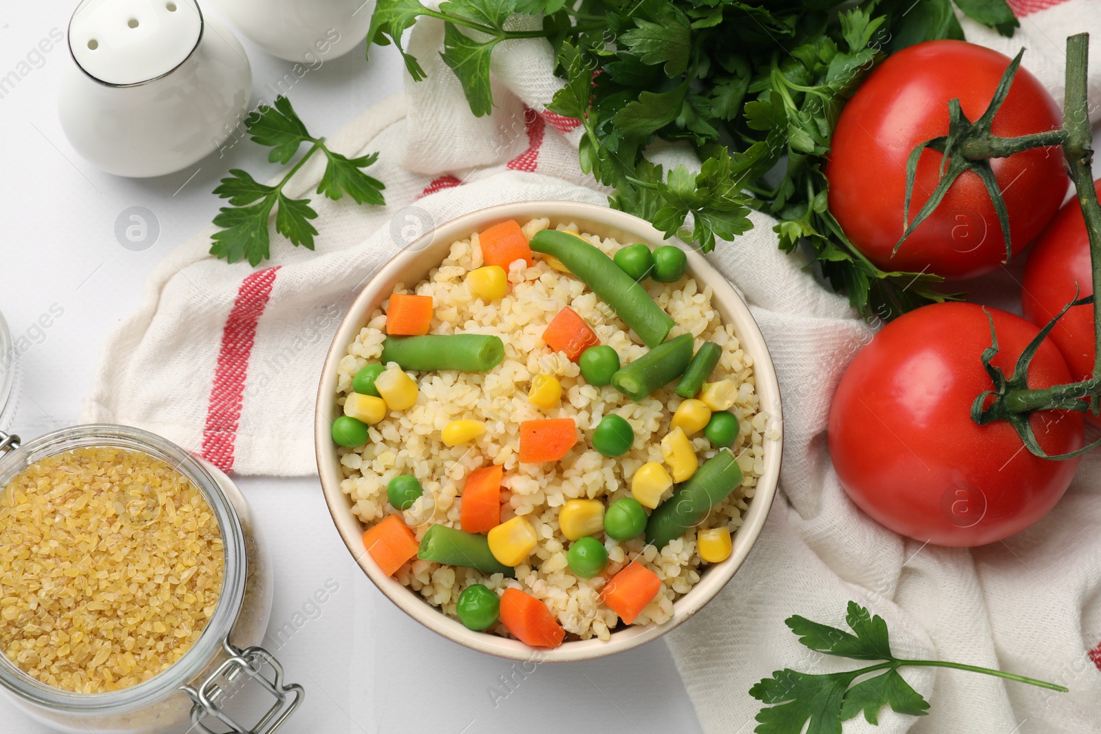 Photo of Delicious bulgur with vegetables in bowl, tomatoes, parsley and spices on table, flat lay