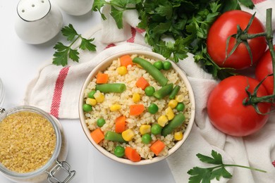 Delicious bulgur with vegetables in bowl, tomatoes, parsley and spices on table, flat lay