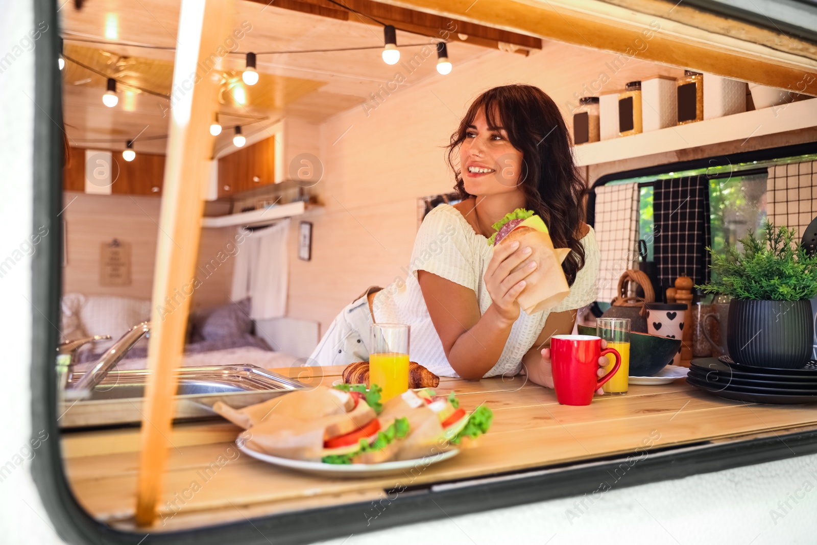 Photo of Young woman having breakfast in trailer, view from outside. Camping vacation