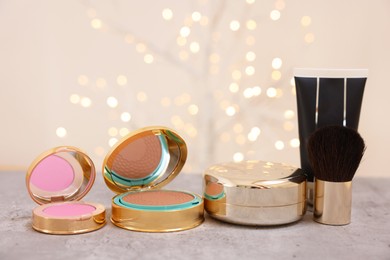 Photo of Face bronzer and other cosmetic products on grey textured table against blurred lights, closeup