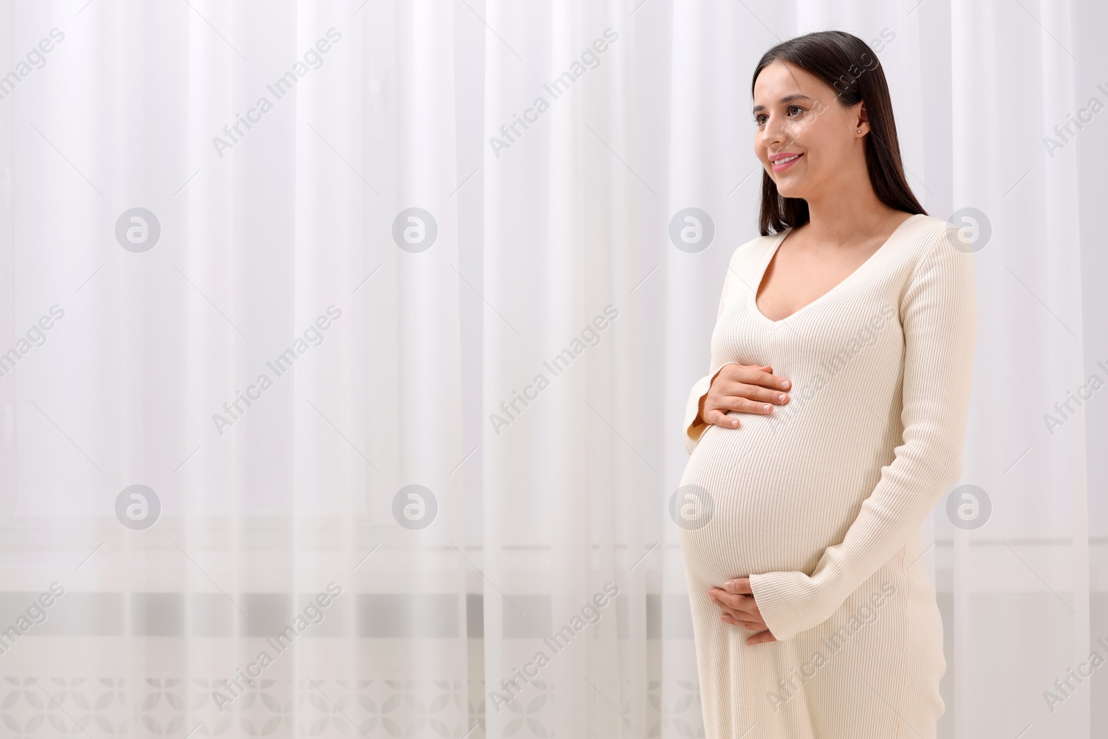 Photo of Beautiful pregnant woman in white dress indoors, space for text