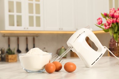 Modern mixer, eggs and bowl with flour on white marble table in kitchen