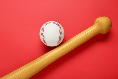 Photo of Wooden baseball bat and ball on red background, flat lay. Sports equipment