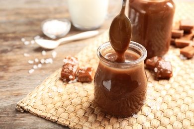 Photo of Spoon of caramel sauce above jar on wooden table. Space for text