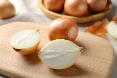 Whole and cut onions on wooden board, closeup