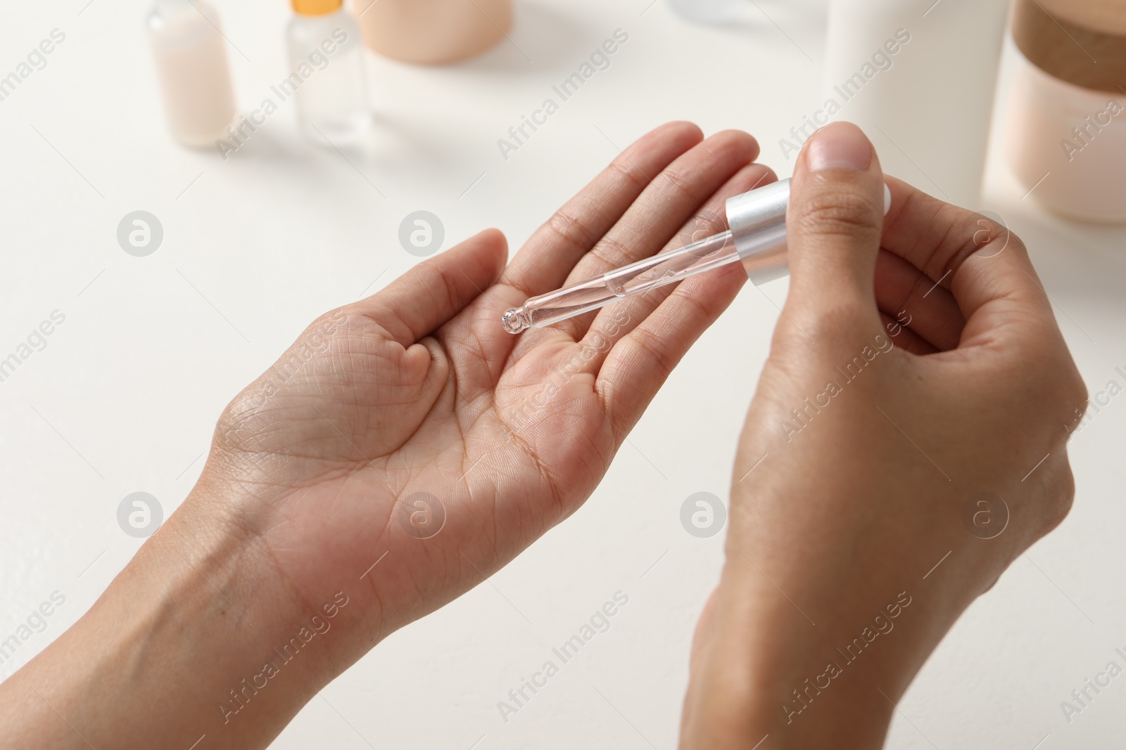 Photo of Woman applying cosmetic serum onto her hand at white table, closeup