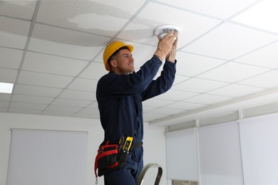 Photo of Electrician in uniform repairing ceiling lamp indoors