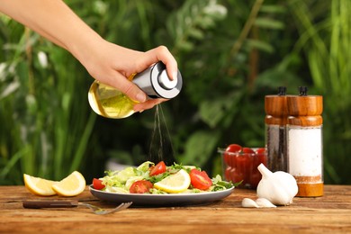 Woman dressing delicious salad with cooking oil at wooden table against blurred background, closeup