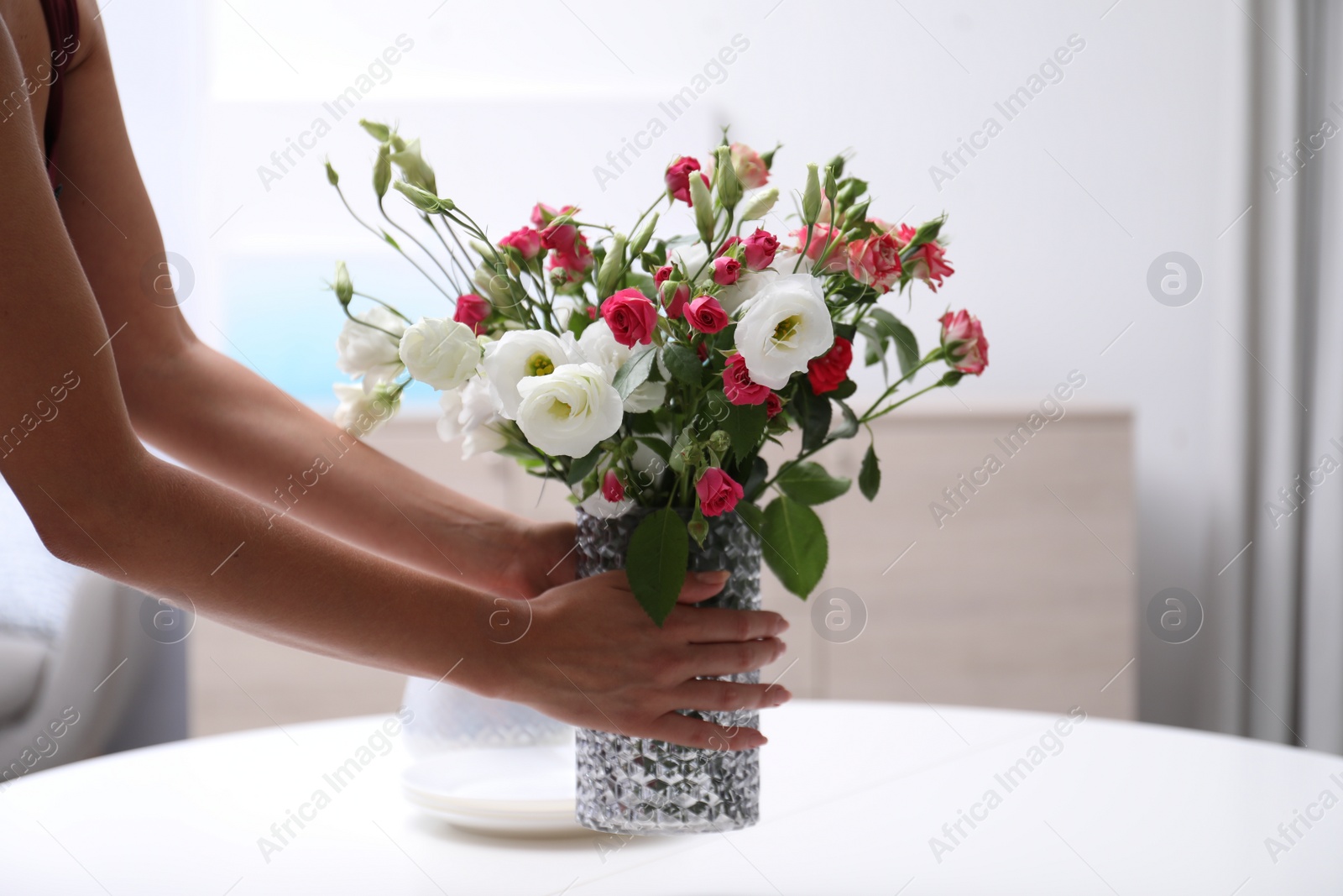 Photo of Woman and vase with beautiful flowers on white table in room, closeup