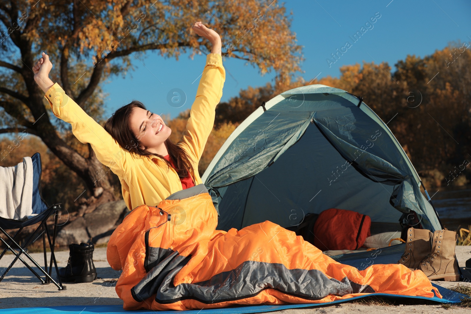 Photo of Woman waking up in sleeping bag near tent outdoors