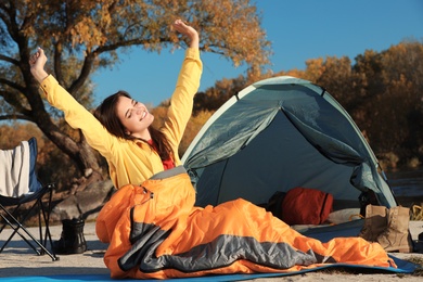 Photo of Woman waking up in sleeping bag near tent outdoors