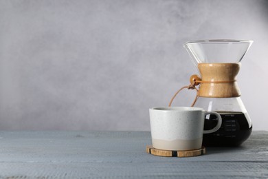 Photo of Glass chemex coffeemaker with tasty drip coffee and cup on grey wooden table. Space for text
