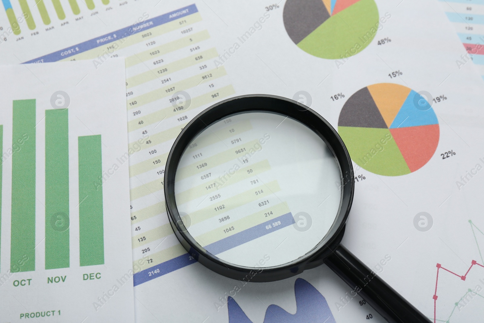 Photo of Magnifying glass on accounting documents with data and graphs, above view