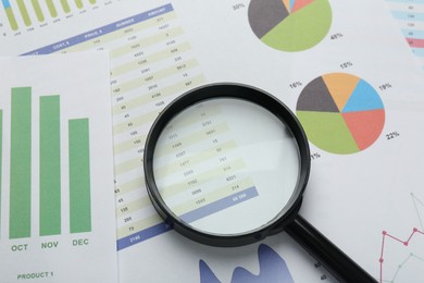 Magnifying glass on accounting documents with data and graphs, above view