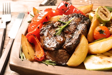 Photo of Delicious barbecued steak served with garnish on wooden board, closeup