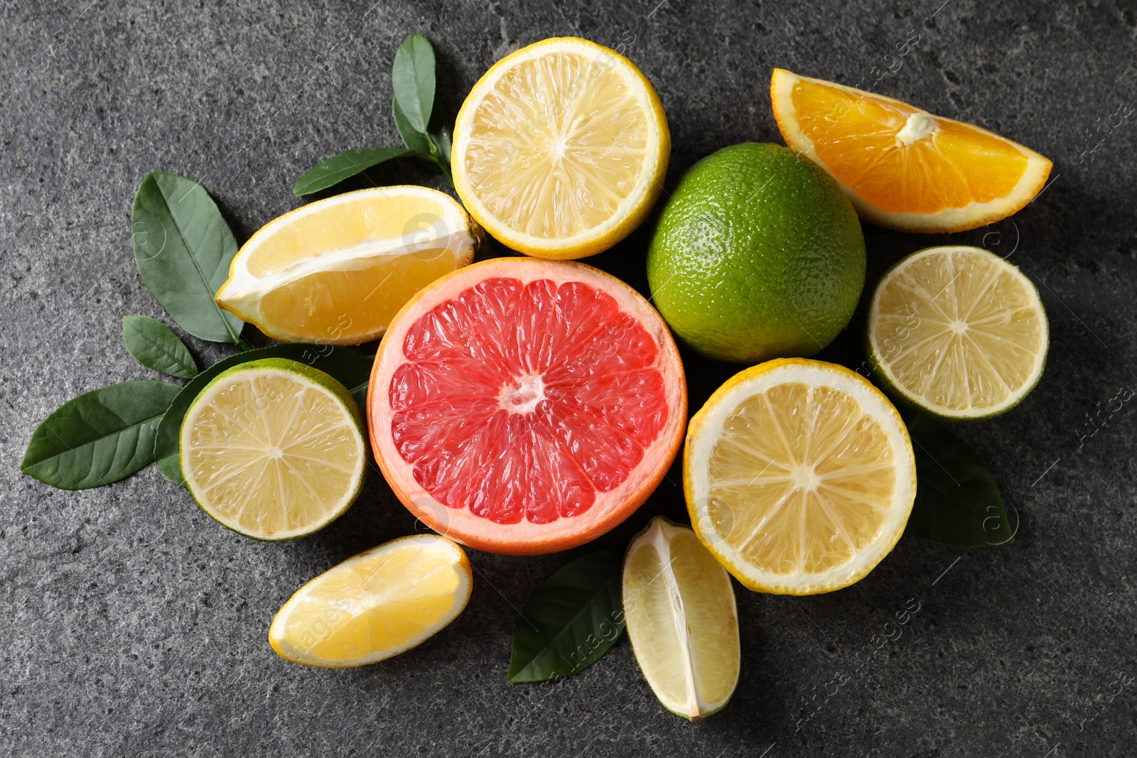 Photo of Different fresh citrus fruits and leaves on grey textured table, flat lay