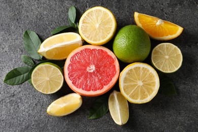 Different fresh citrus fruits and leaves on grey textured table, flat lay