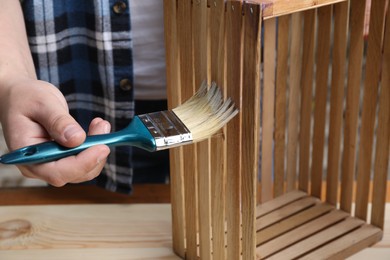 Man applying varnish onto wooden crate at table, closeup