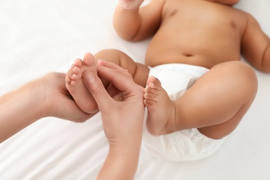 Photo of Mother and her cute child on white bed, closeup. Baby massage and exercises