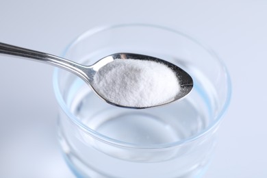 Photo of Spoon with baking soda over glass of water on light background, closeup