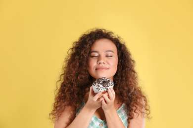 Photo of Beautiful African-American woman with donut on yellow background