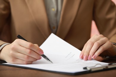 Woman signing documents at wooden table in office, closeup