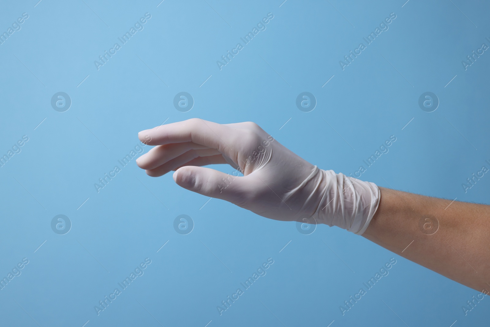 Photo of Doctor wearing white medical glove on light blue background, closeup