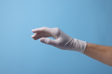 Photo of Doctor wearing white medical glove on light blue background, closeup