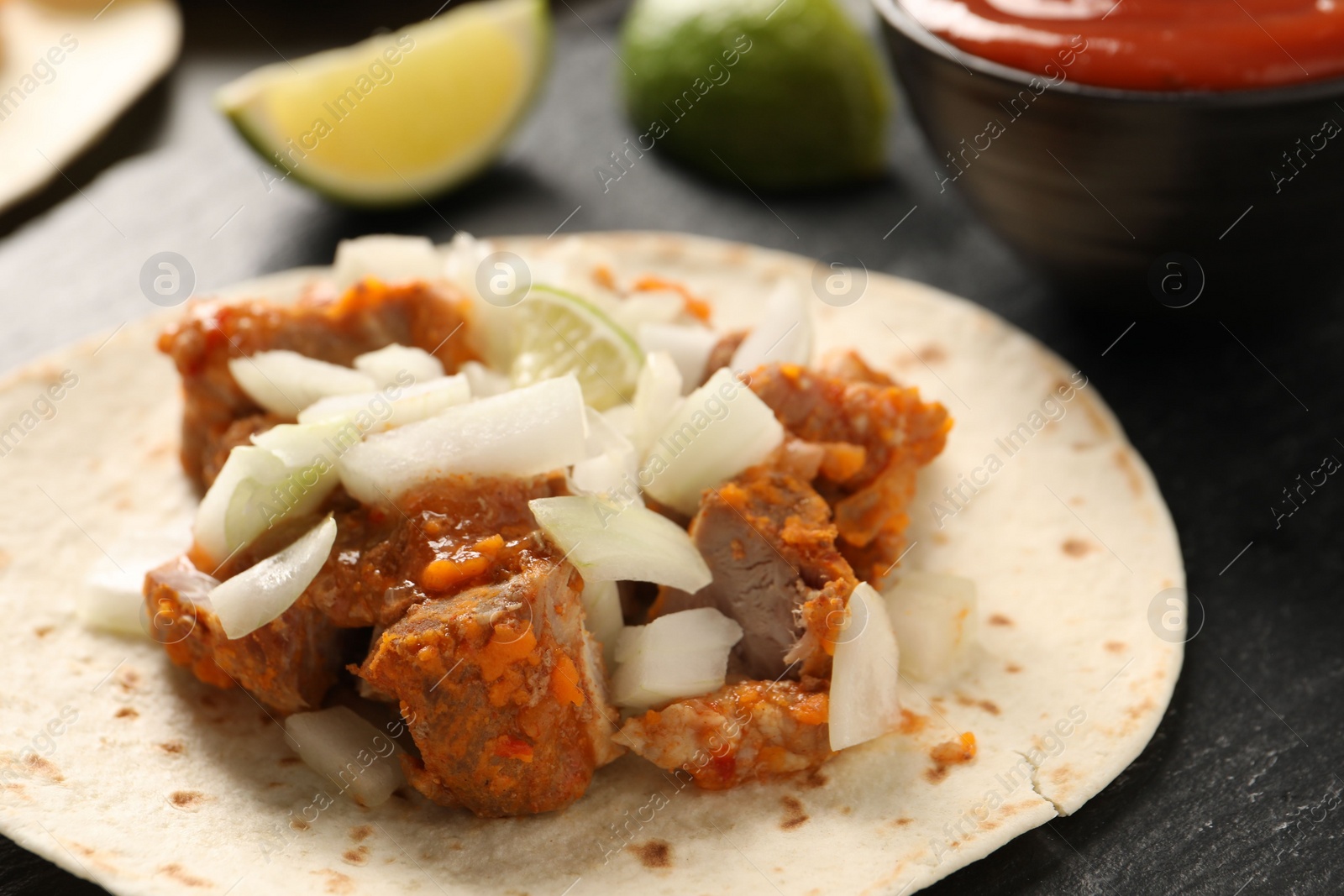 Photo of Delicious taco with vegetables, meat and lime on dark textured table, closeup