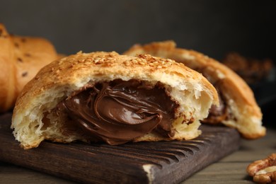 Tasty croissant with chocolate and sesame seeds on wooden board, closeup
