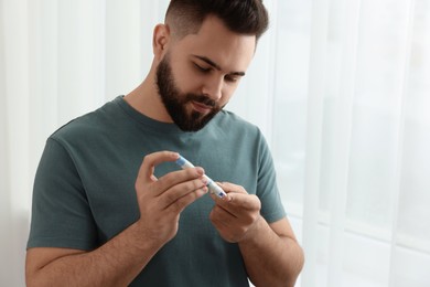 Photo of Diabetes test. Man checking blood sugar level with lancet pen at home