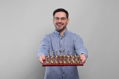 Smiling man holding chessboard with game pieces on light grey background