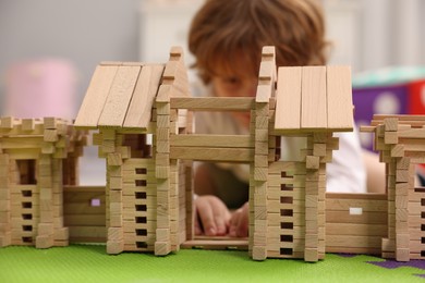 Photo of Little boy playing with wooden entry gate on puzzle mat in room, selective focus. Child's toy