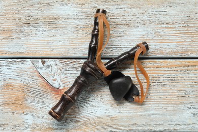 Photo of Black slingshot with pebble on old light blue wooden table, top view
