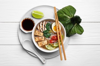 Delicious vegetarian ramen, soy sauce and pak choy leaves on white wooden table, top view