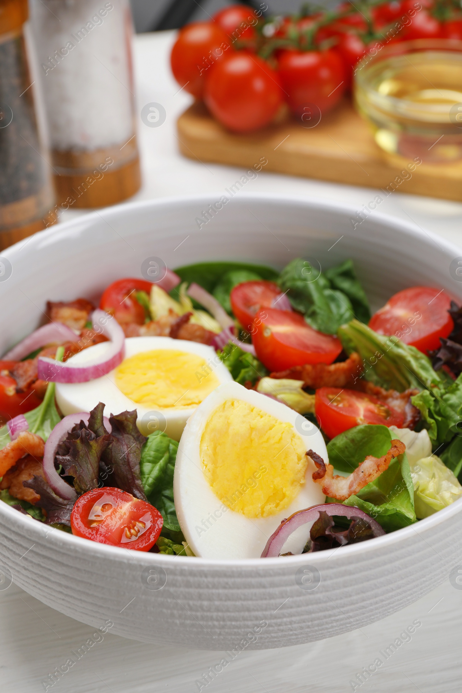 Photo of Delicious salad with boiled egg, bacon and vegetables on white table, closeup
